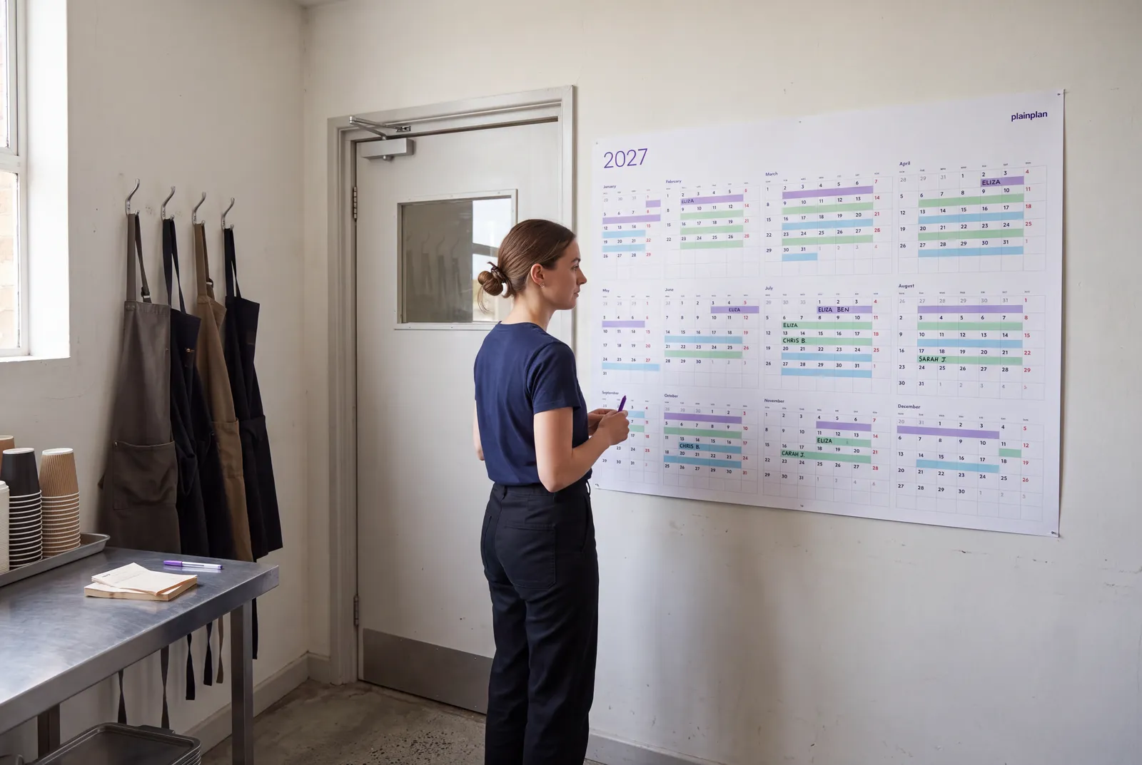 Cafe manager checking the staff shift plan on a plainplan 2027 wall planner