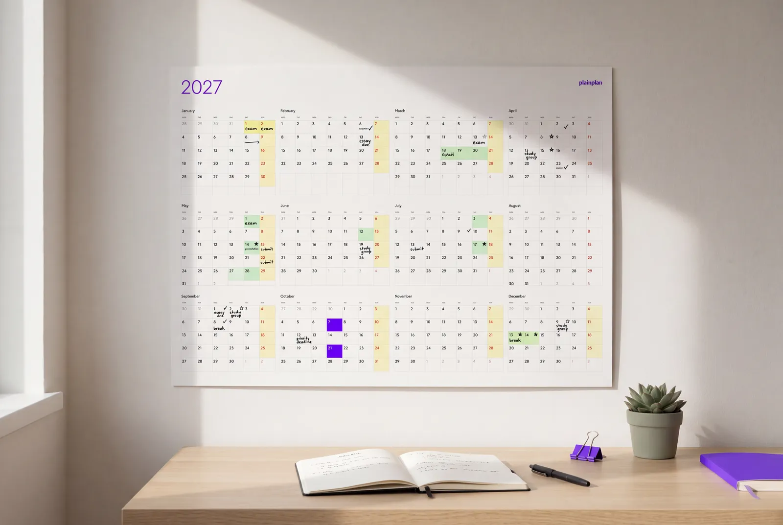 Yearly wall planner color-coded with markers and sticky notes above a study desk